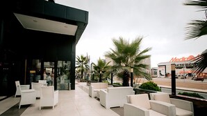 An outdoor seating area with white wicker furniture and a view of a commercial building in the background. - KONAK PARK HOTEL (Yomra)