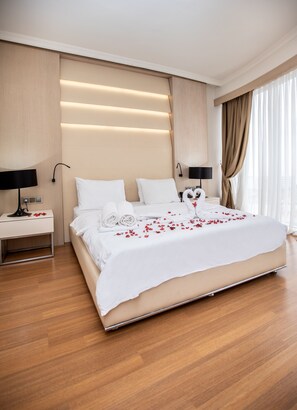 A modern hotel bedroom with a large bed, two bedside tables, and a view of the city through sheer curtains. - KONAK PARK HOTEL (Yomra)