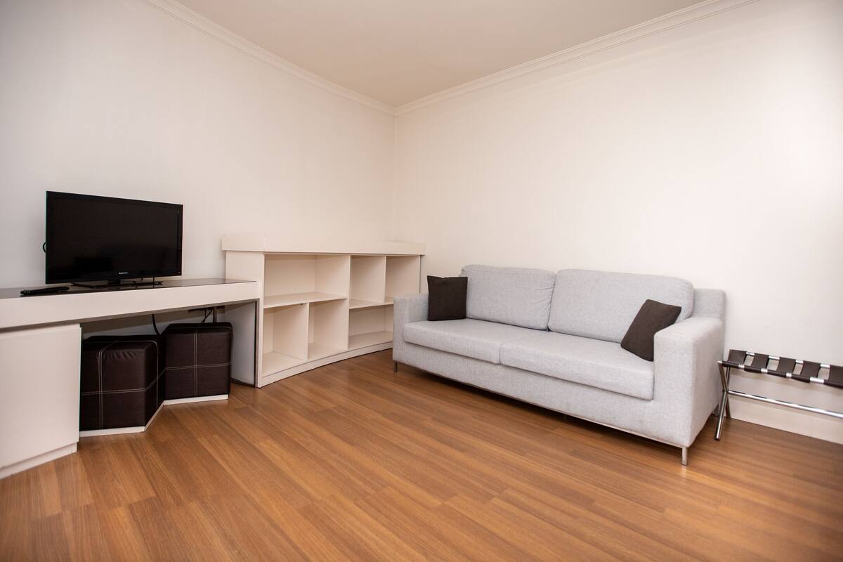 Una sala moderna con un televisor de pantalla plana, un sofá gris y suelo de madera.