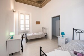 Un dormitorio con dos camas, una ventana, un radiador, un escritorio y una mesita de noche.