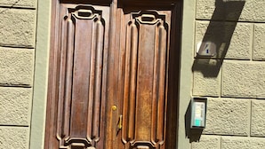 A wooden double door with intricate carvings, set in a stone wall with a small electrical box attached to the right side. - Campidoglio (Florence)
