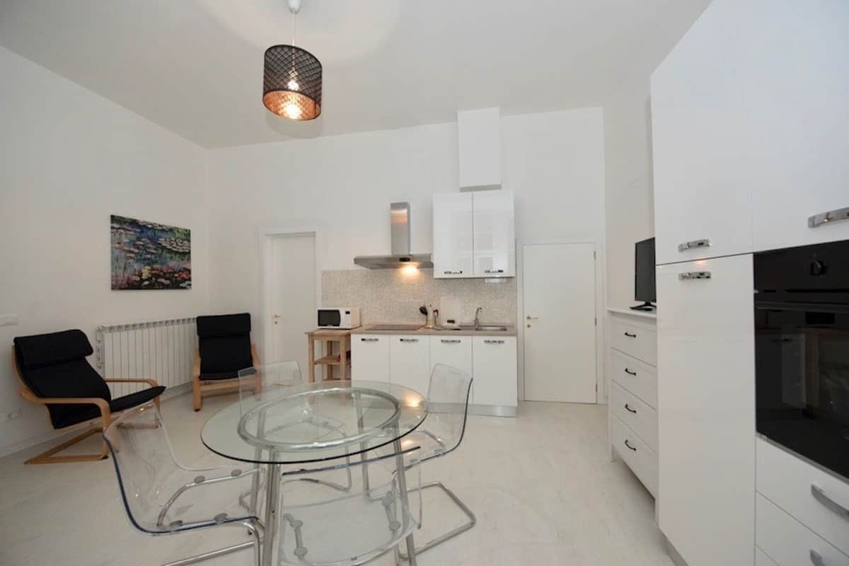 A modern kitchen with white cabinets, a glass dining table, and a black chair.
