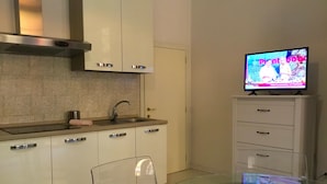 A modern kitchen with a glass dining table, a built-in oven, and a television on a cabinet. - Campidoglio (Florence)