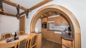 A kitchen with wooden cabinets, a dining table with chairs, and a built-in oven. - Wellness Appartementhaus Seebichl (Nesselwaengle)