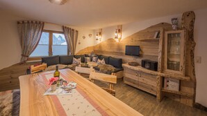 A cozy living room with a wooden sofa, a dining table with a vase of flowers, and a wooden cabinet with glass doors. - Wellness Appartementhaus Seebichl (Nesselwaengle)