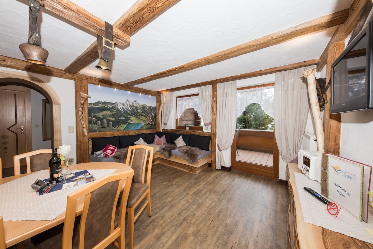 Una habitación acogedora con techo de madera, una mesa de comedor con sillas, un sofá, un televisor y una vista panorámica de la montaña a través de la ventana.
