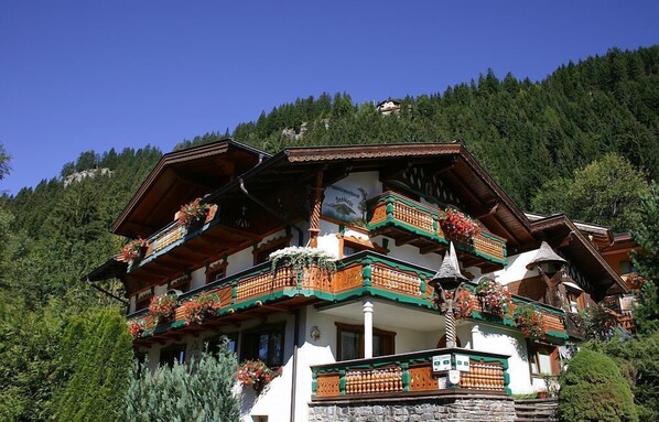 A traditional chalet with multiple balconies adorned with flowers, set against a mountainous backdrop.