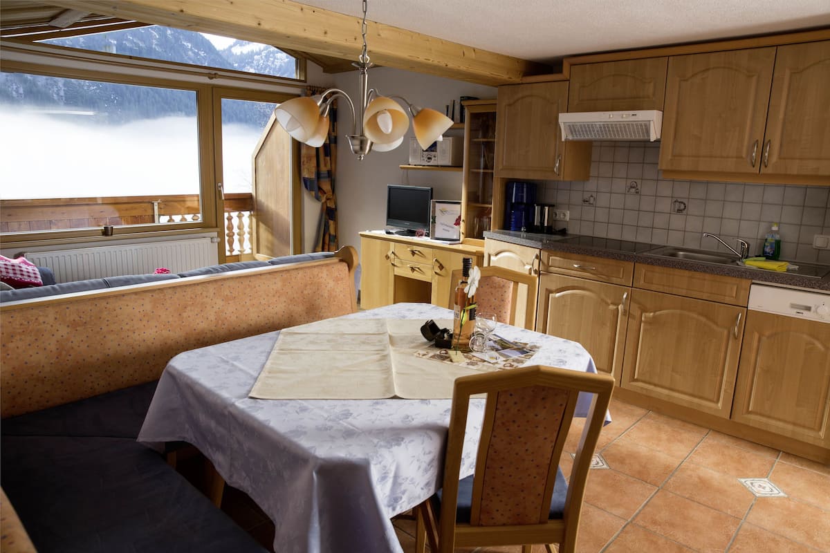 Una cocina acogedora con armarios de madera, una mesa de comedor con mantel y vistas a las montañas a través de un ventanal.