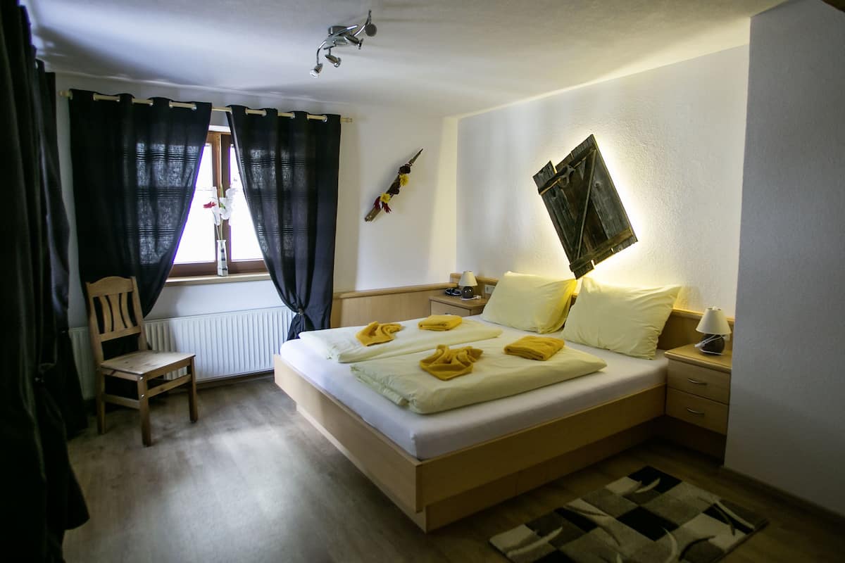 Una habitación de hotel con cama, una silla, una mesita de noche, una lámpara y una ventana con cortinas.