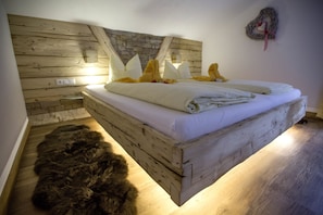 A bed with a wooden headboard, a fur rug, and a wall with a woven decoration.