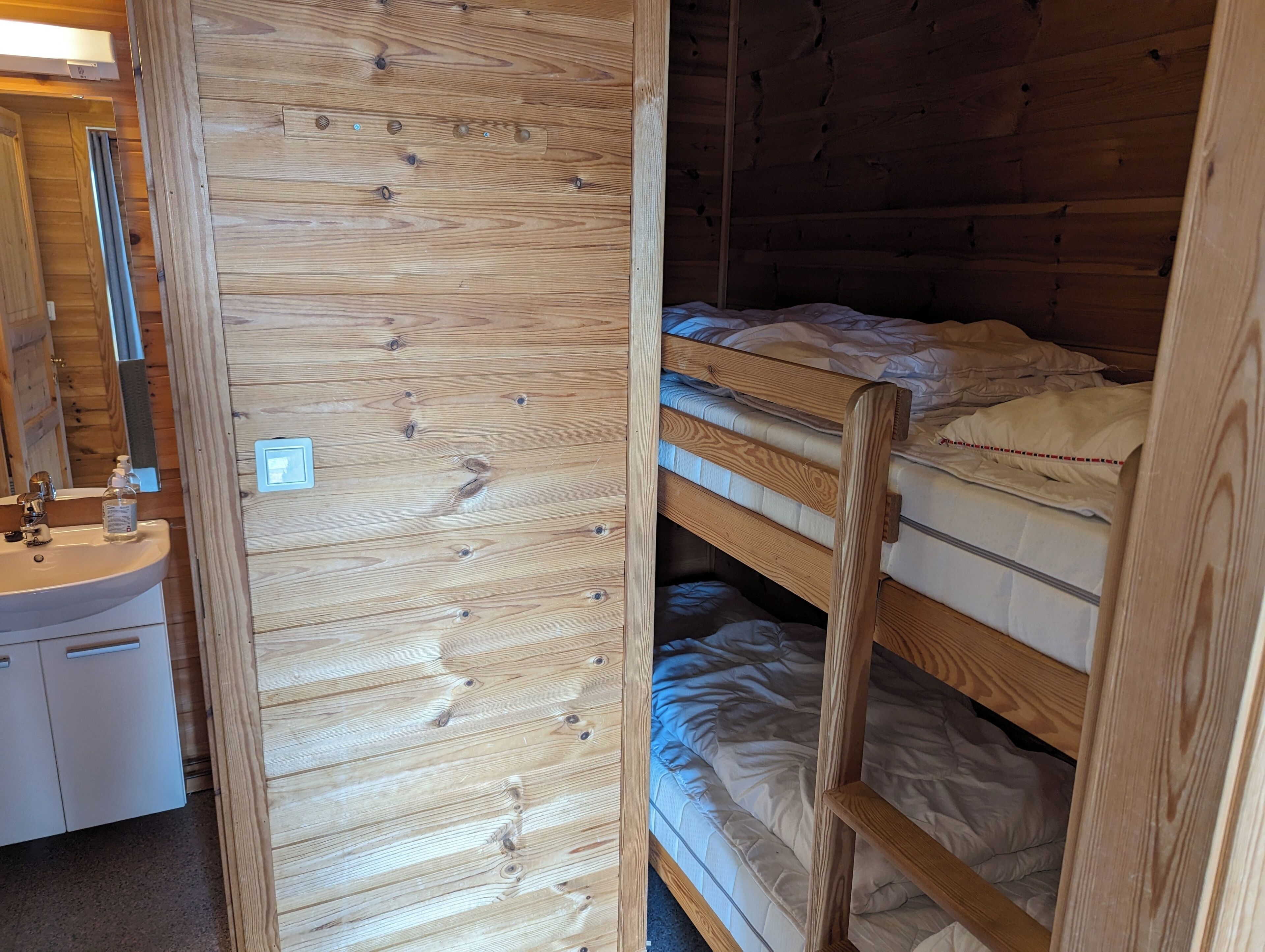 Een slaapkamer met stapelbed, een houten wand, een wastafel en een spiegel.