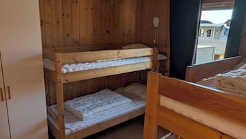 A bunk bed room with wooden walls, a white wardrobe, and a window with curtains.