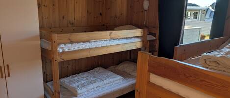 A bunk bed room with wooden walls, a white wardrobe, and a window with curtains.