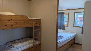 A room with bunk beds, a window with curtains, and a wooden floor.