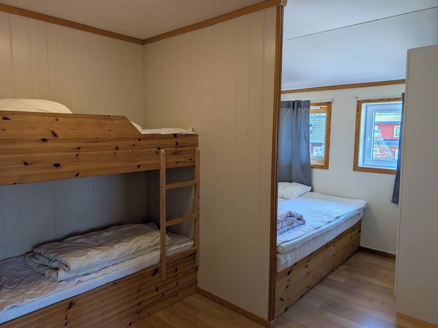 A room with bunk beds, a window with curtains, and a wooden floor.