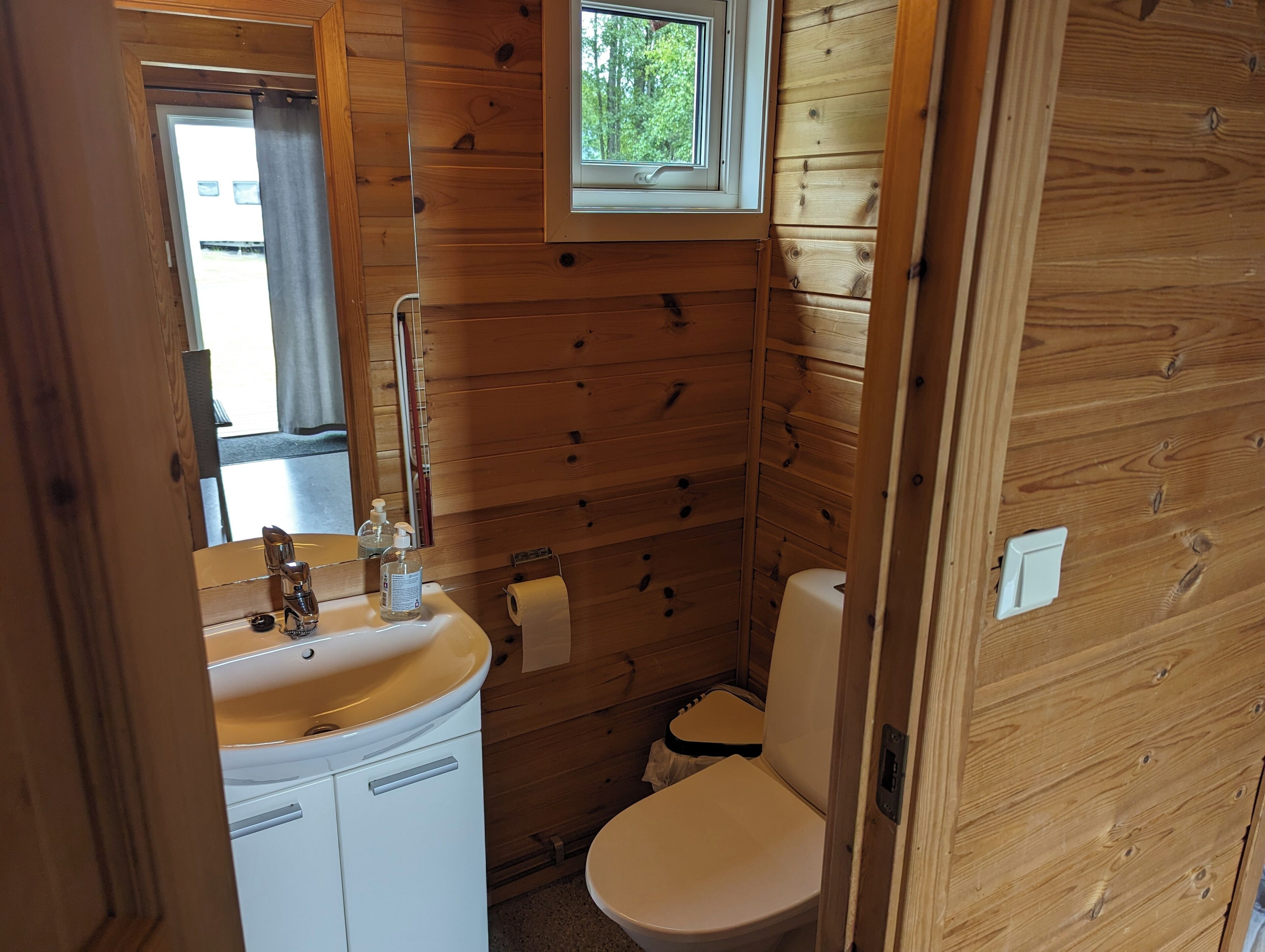 A wooden cabin bathroom with a sink, toilet, and window.