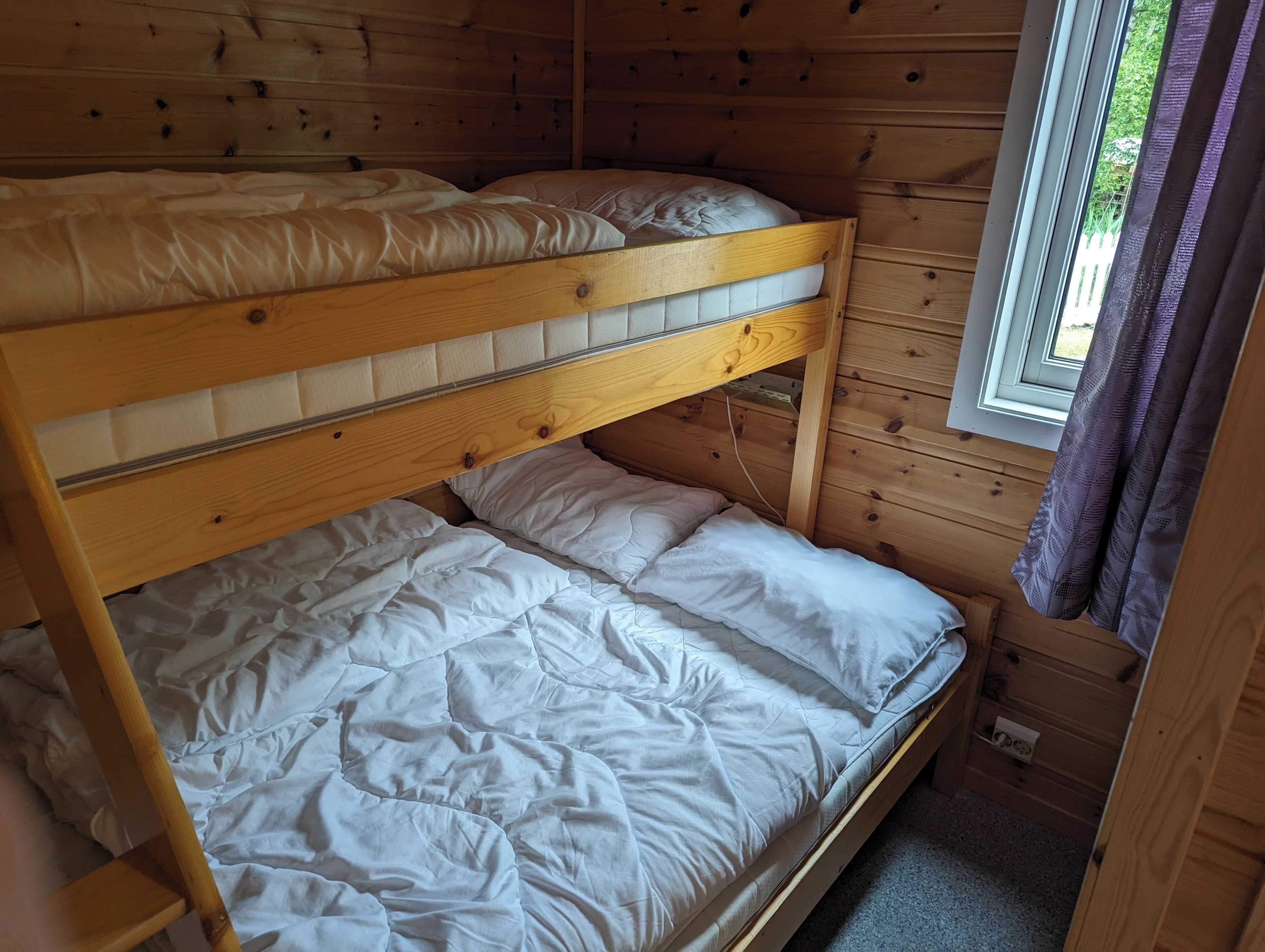 Una cama litera con ropa de cama blanca en una habitación tipo cabaña de madera.