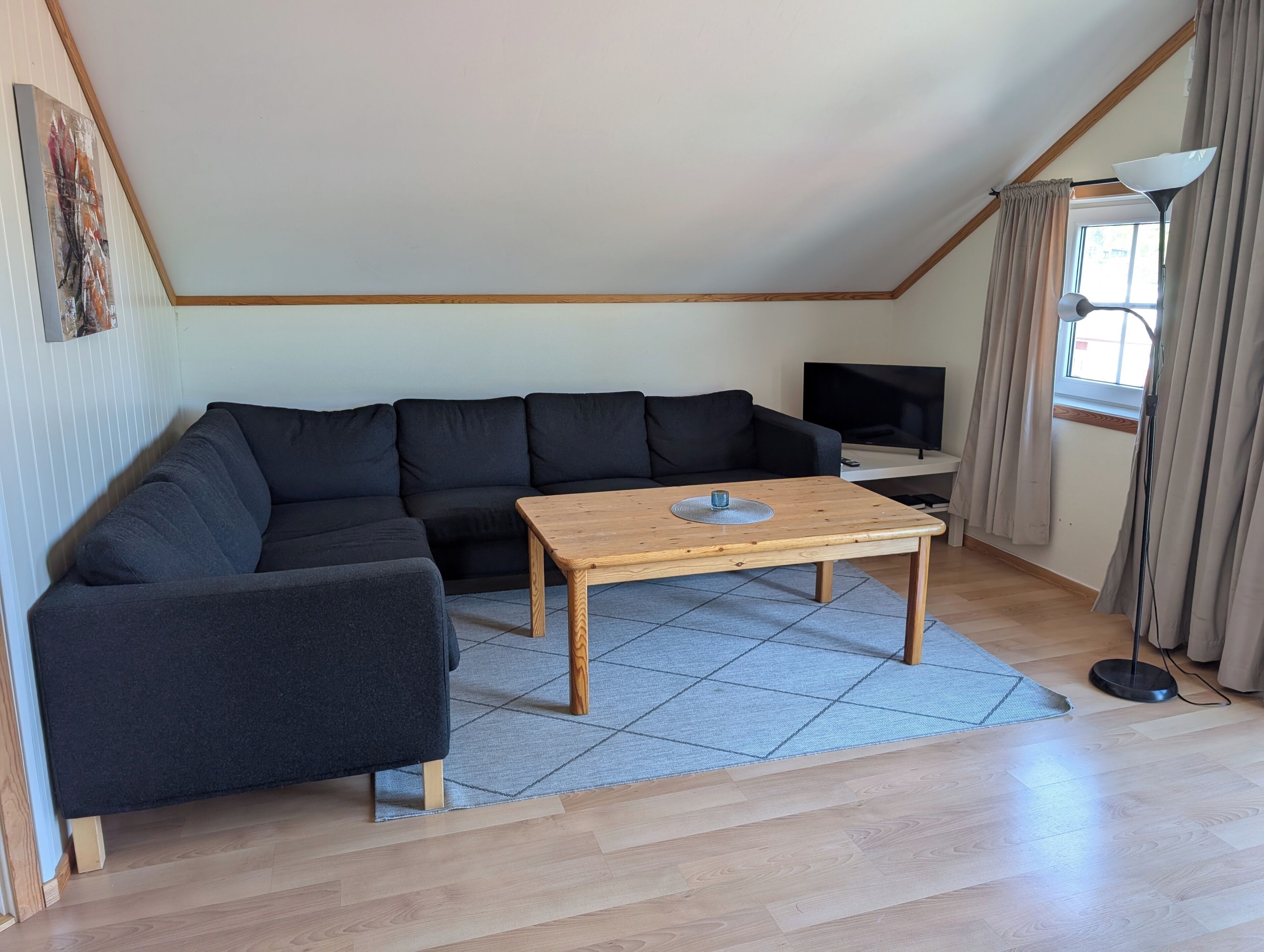 A living room with a sectional sofa, a wooden coffee table, a TV, and a window with curtains.