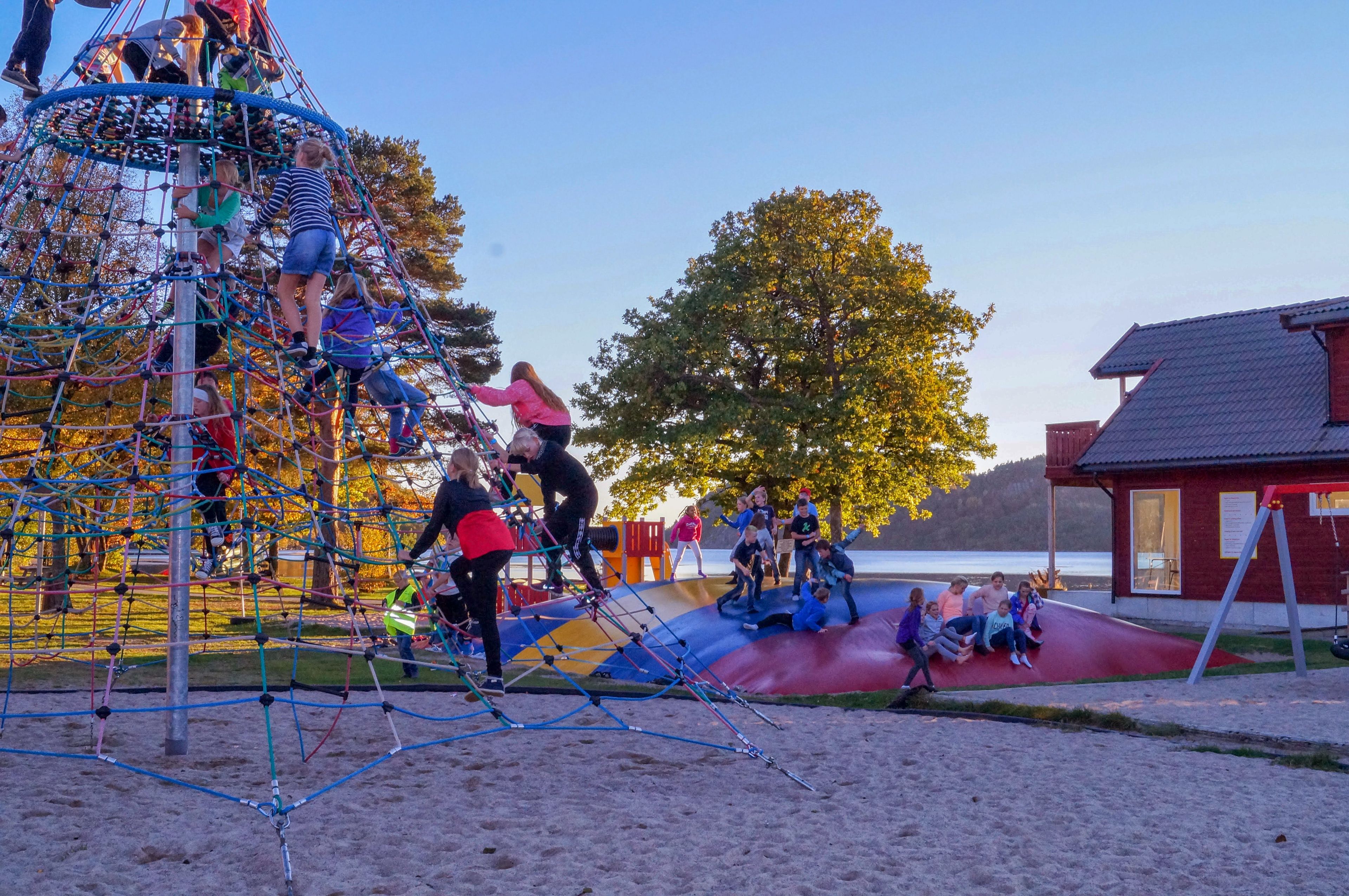 A playground with climbing structures and slides, surrounded by trees and a building with a red roof.
