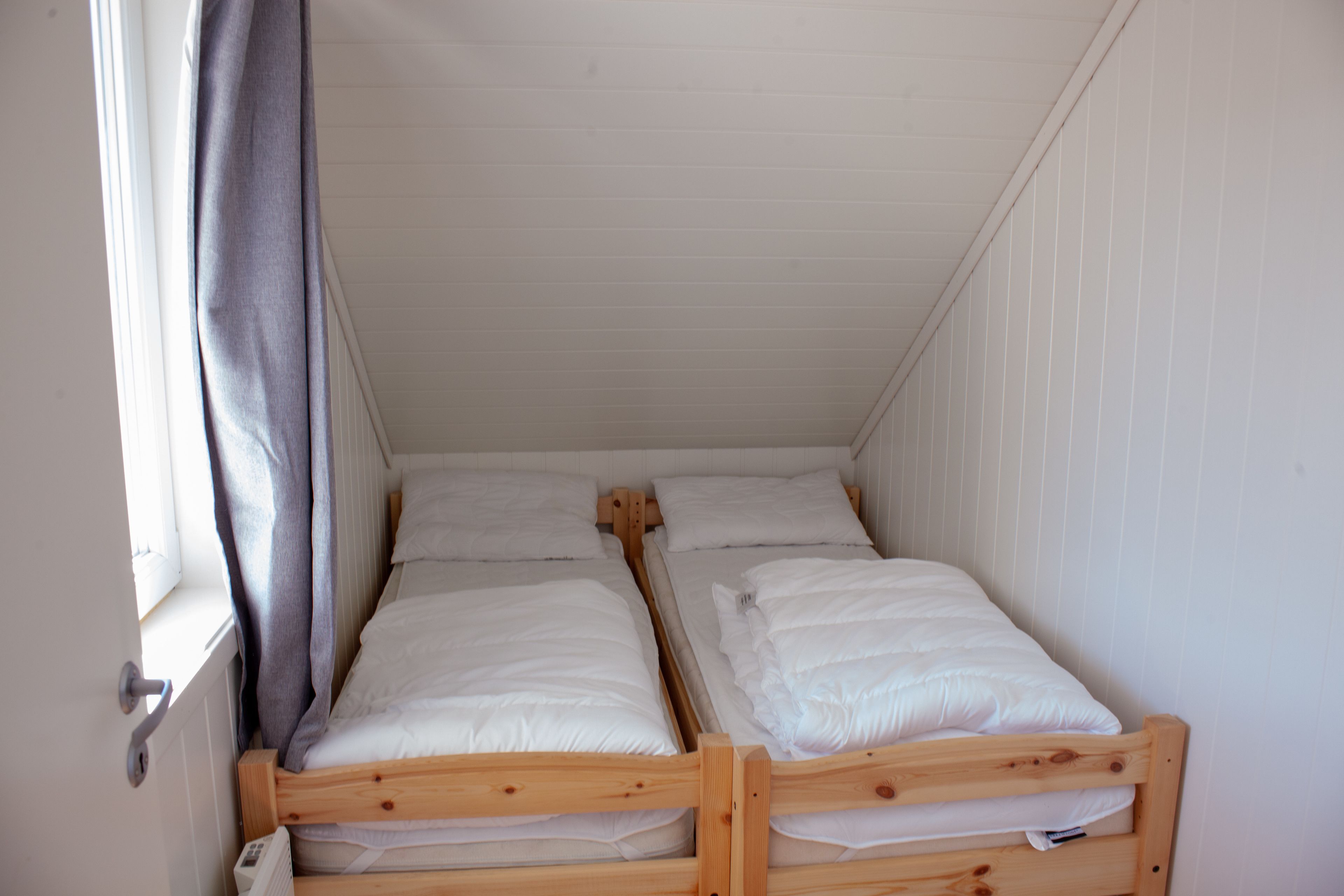 Een kleine, compacte kamer met twee houten stapelbedden, witte wanden en een raam met gordijn.