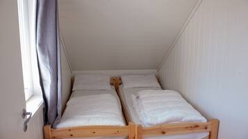 Een kleine, compacte kamer met twee houten stapelbedden, witte wanden en een raam met gordijn.