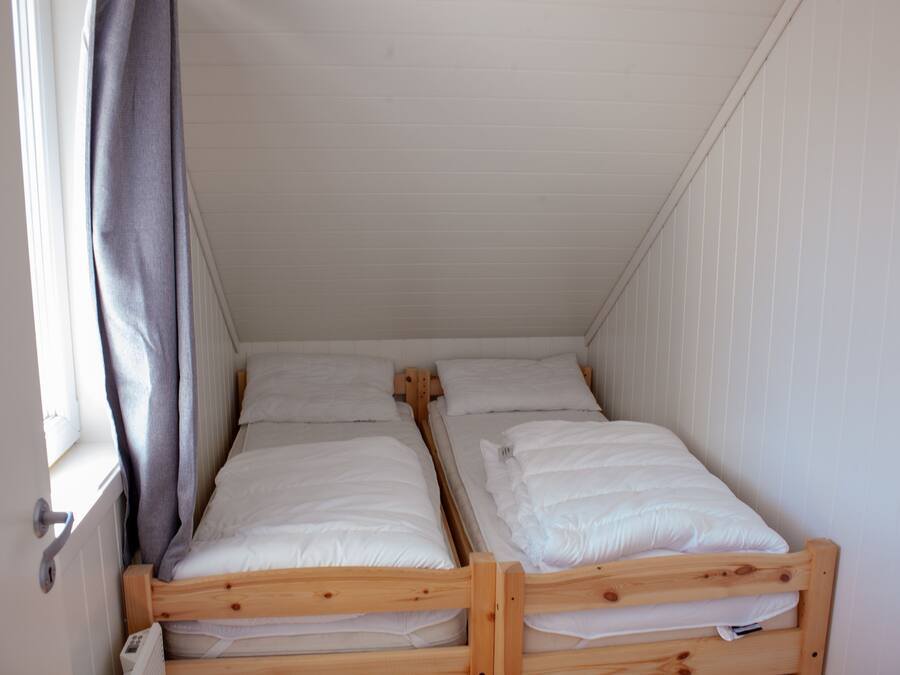 Een kleine, compacte kamer met twee houten stapelbedden, witte wanden en een raam met gordijn.