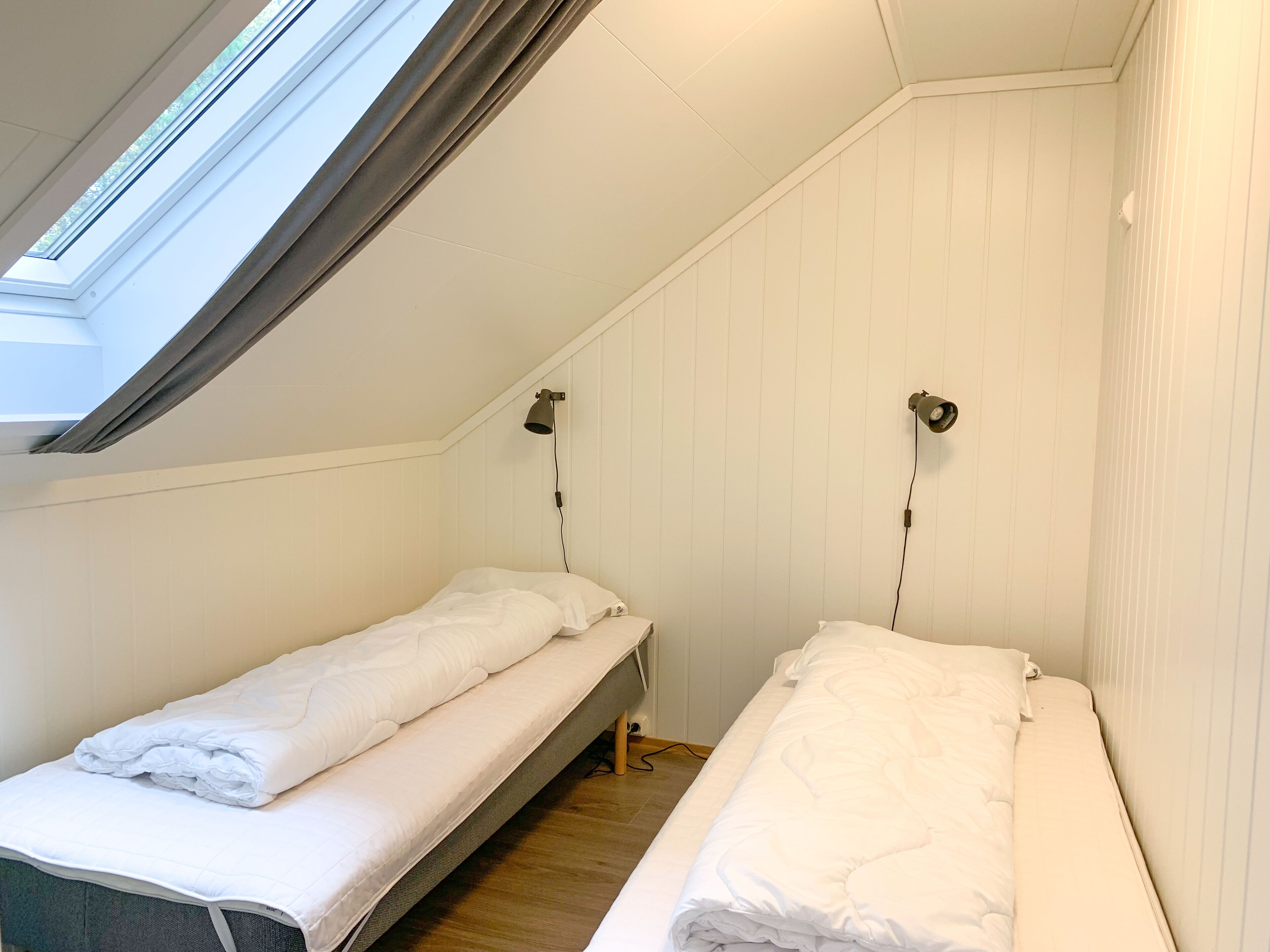 A small, single-room with two beds, a skylight, and a sloped ceiling.