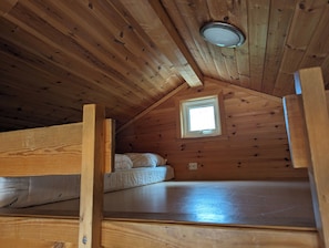 A wooden cabin with a loft bedroom, a small window, and a ceiling light. - Solstrand Camping (Lindesnes)