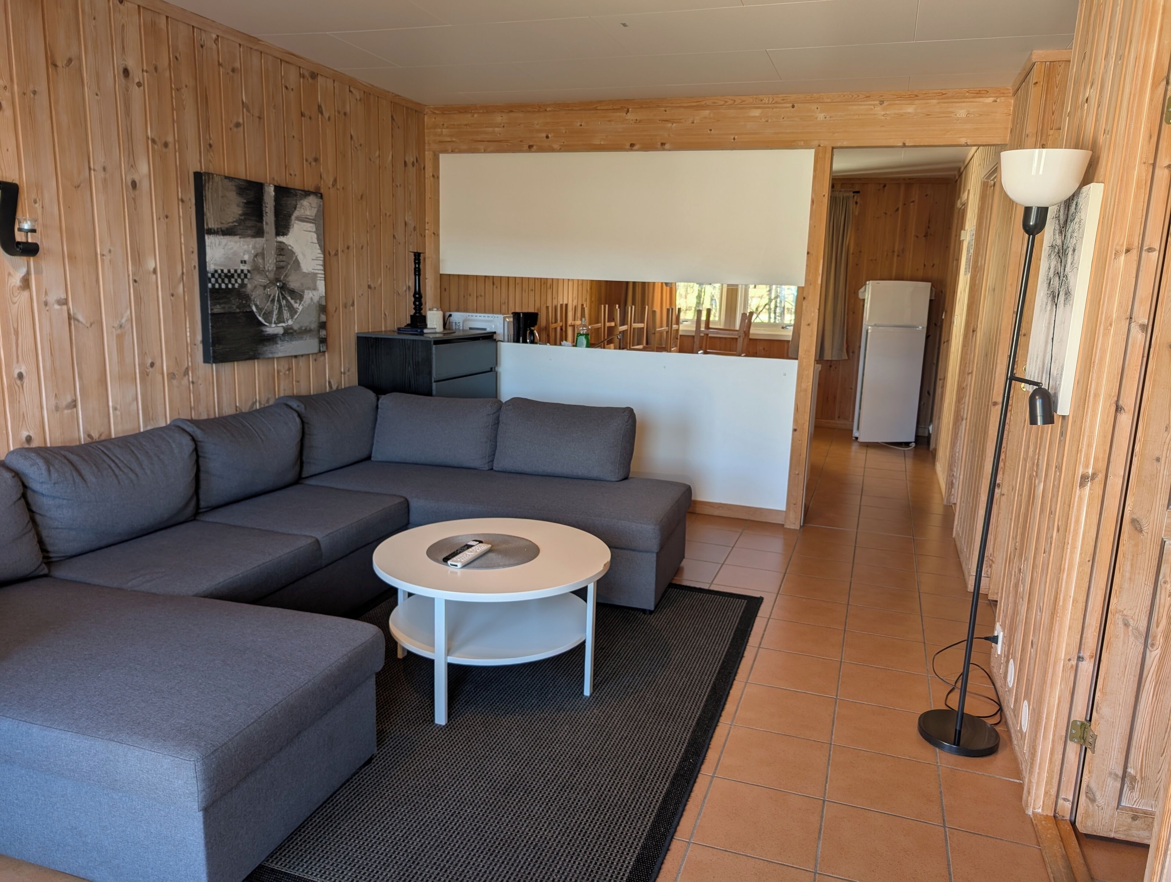 Ein modernes Wohnzimmer mit einer Eckcouch, einem kleinen runden Tisch und einer Küchenzeile im Hintergrund.