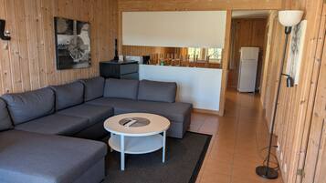 Ein modernes Wohnzimmer mit einer Eckcouch, einem kleinen runden Tisch und einer Küchenzeile im Hintergrund.