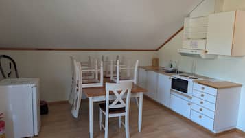 A compact kitchen with white cabinets, a wooden dining table with chairs, a small refrigerator, and a gas stove.