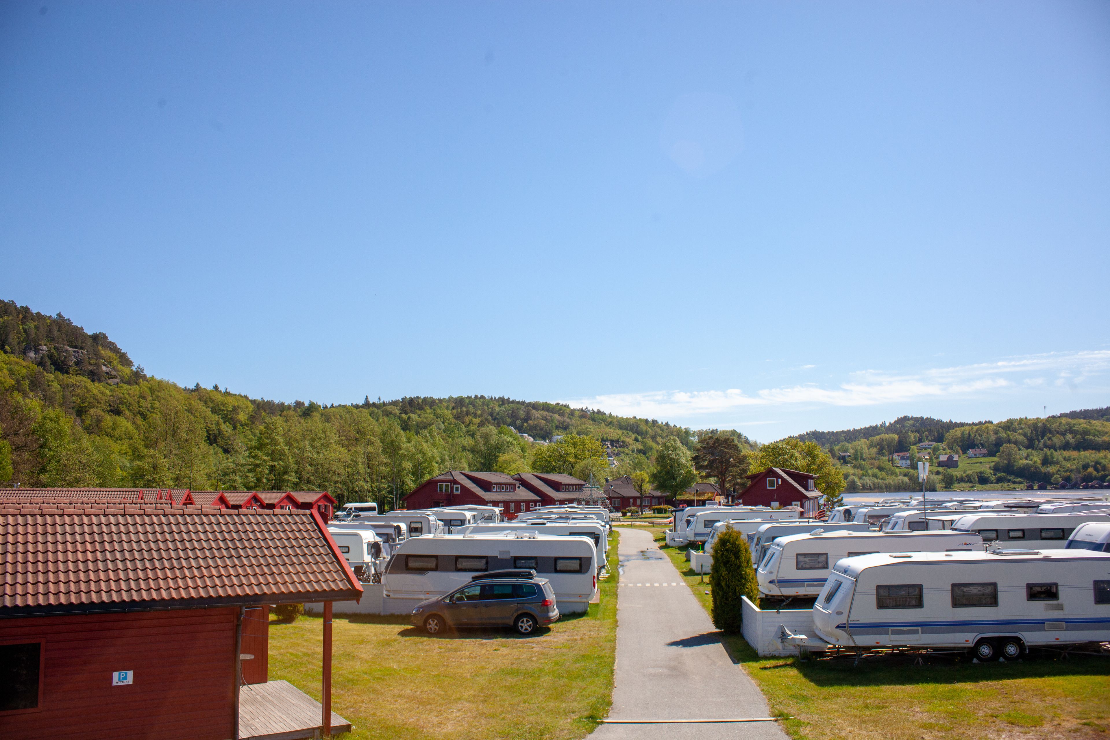 Leirintäalue, jossa matkailuautot on pysäköity riveihin, punainen rakennus ja polku, joka kulkee alueen läpi.