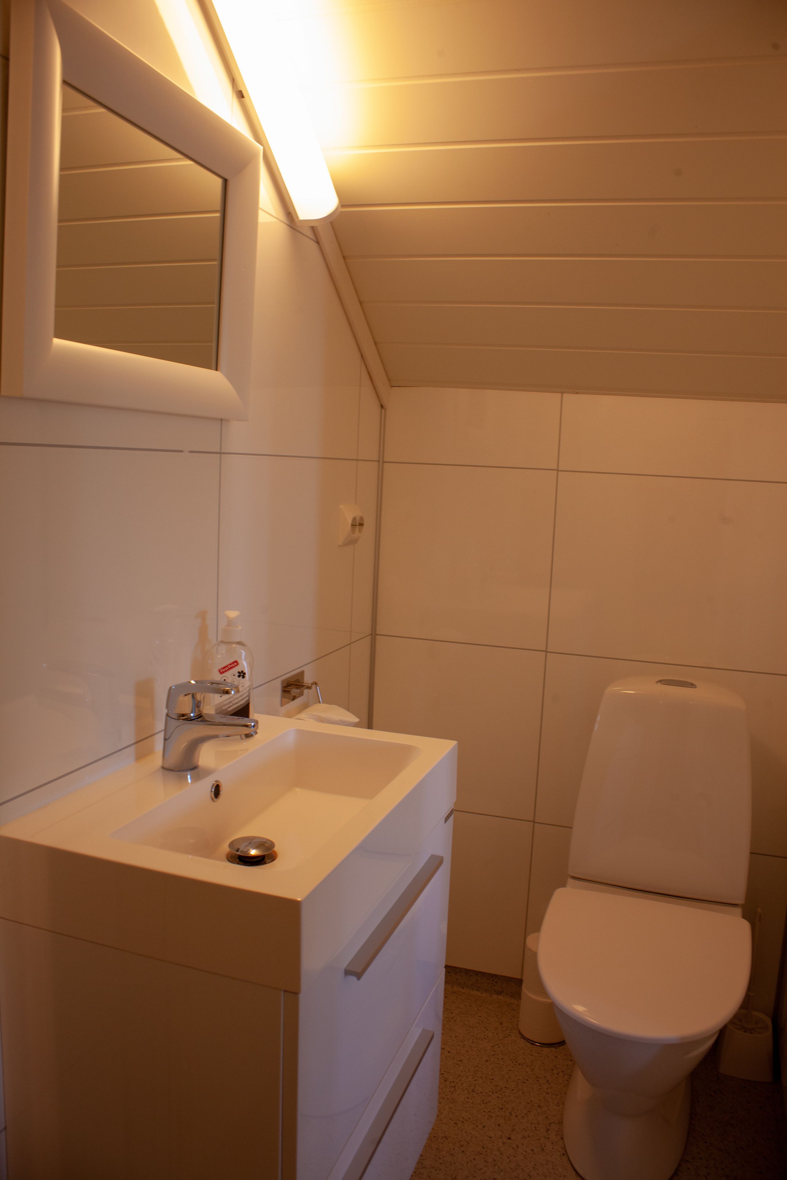A small, modern bathroom with a white sink, mirror, and toilet.