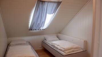 Eine kleine Einzimmerwohnung mit schrägem Dach, einem Fenster mit Vorhang und zwei Betten.