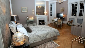A bedroom with a large bed, a desk, a television, and a fireplace.