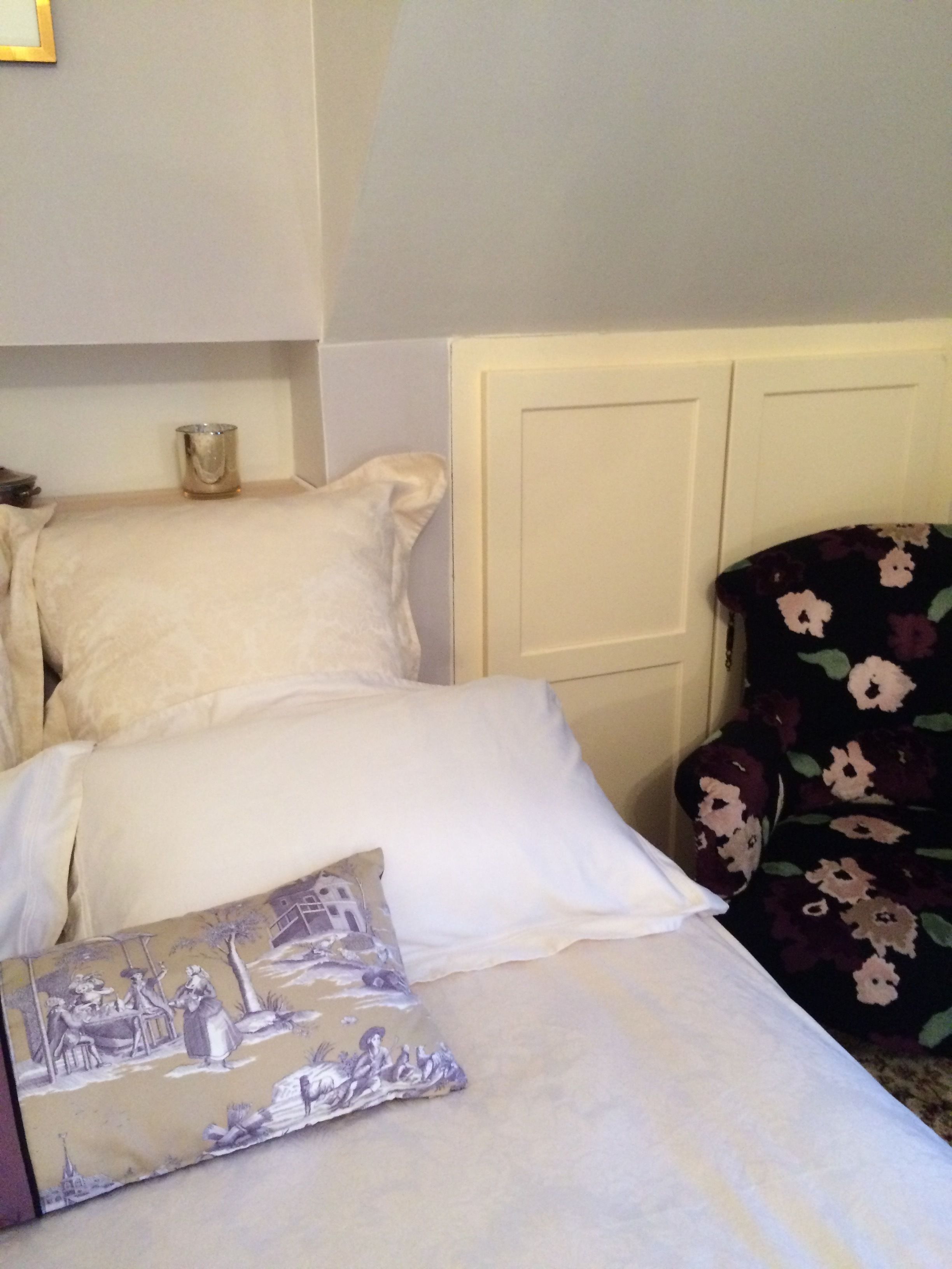 A bedroom with a bed, pillows, a decorative pillow, a nightstand, and a chair with a floral pattern.