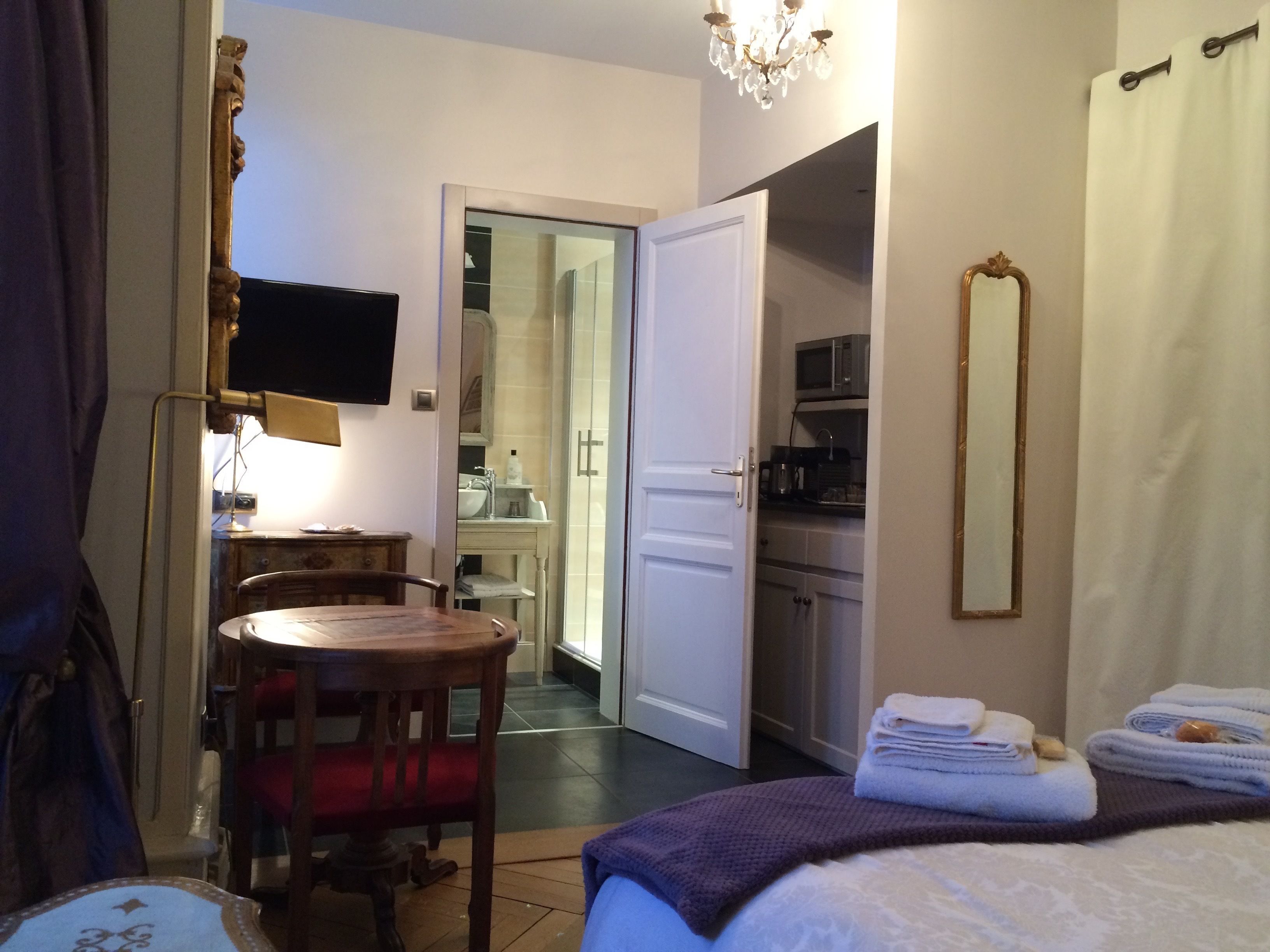 Habitación de hotel con cama, escritorio, silla, televisor, espejo y baño visible a través de una puerta abierta.