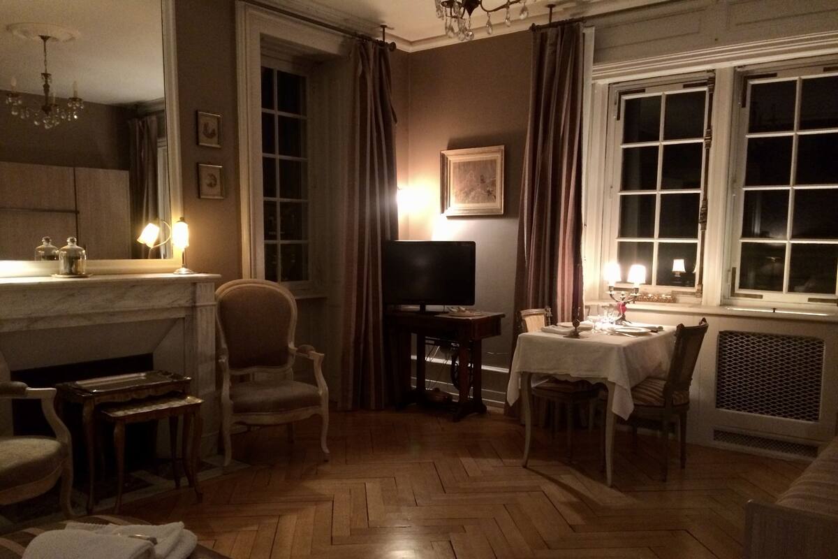 Une pièce faiblement éclairée, avec une cheminée, un téléviseur et une table à manger dressée pour deux personnes.