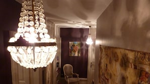 A hallway with a chandelier, a chair, and a wall with artwork.