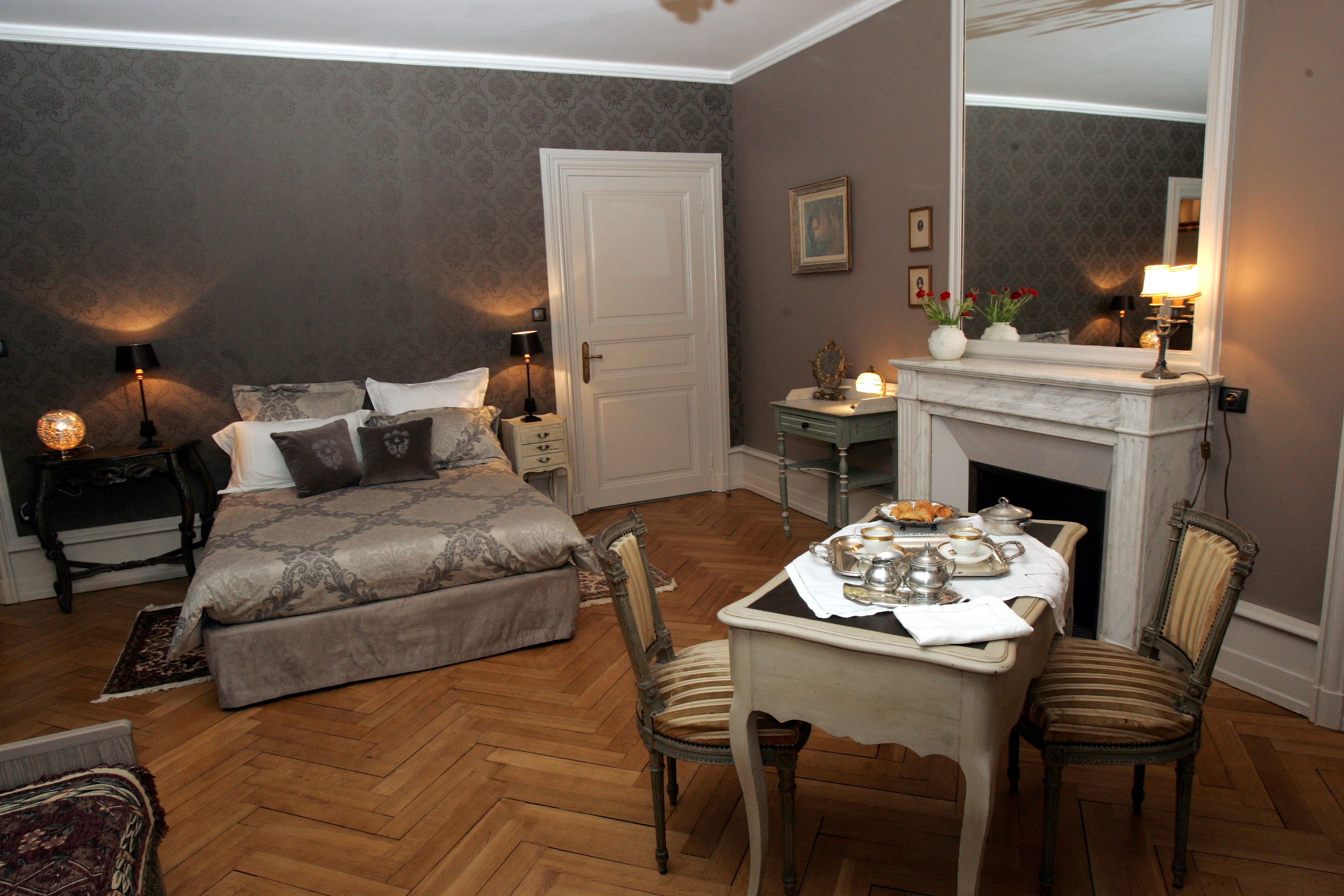 Un dormitorio con cama, mesitas de noche, cómoda, espejo y chimenea.
