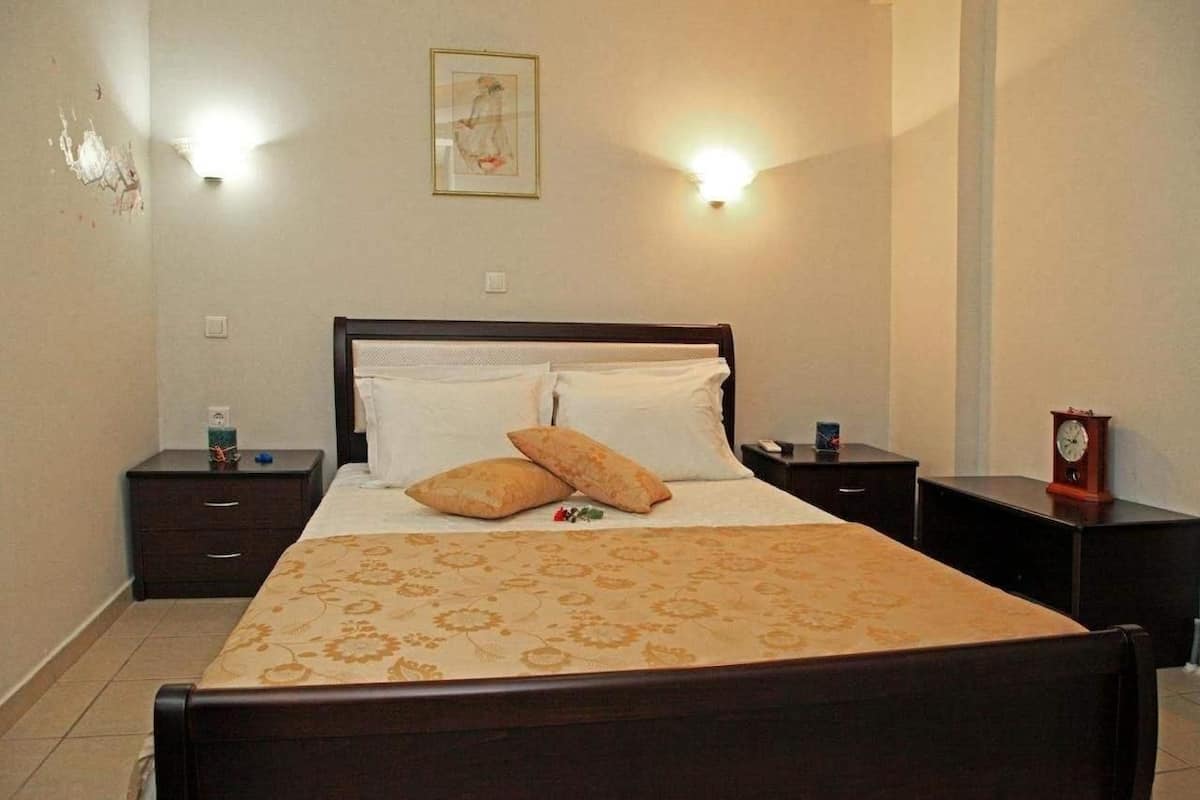 A neatly made bed with a floral bedspread, two pillows, and a nightstand with a clock and a bottle.