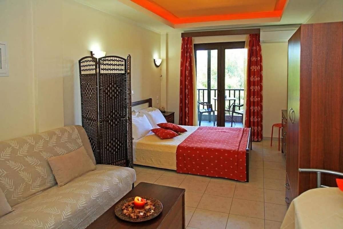 A hotel room with a bed, a sofa, a dining table with a plate of food, a decorative screen, and a balcony with a chair.