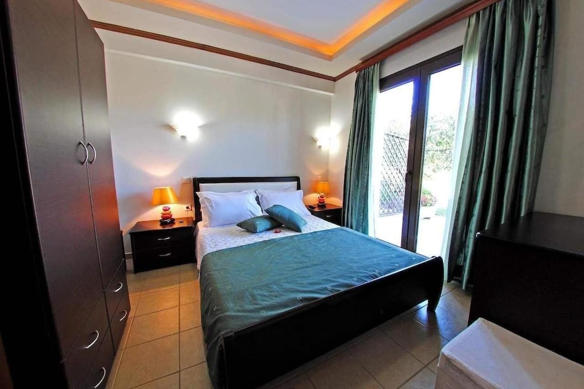 A bedroom with a bed, two bedside tables with lamps, a wardrobe, and a view of the outdoors through a sliding door.