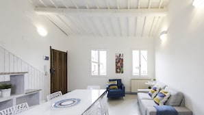 A spacious living area with a white ceiling, a dining table with chairs, a sofa, and a radiator.
