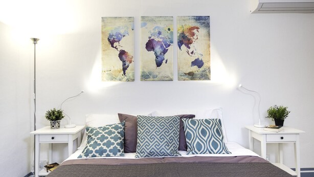 A bedroom with a bed, two bedside tables, a floor lamp, and three wall-mounted abstract paintings.
