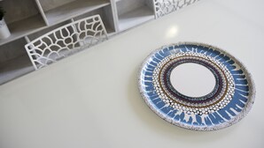 A white table with a decorative plate and two white, intricately designed wall shelves.