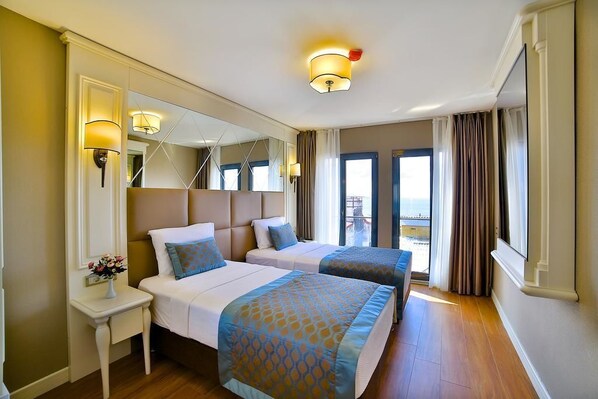A hotel room with two beds, a large mirror, a nightstand with a vase of flowers, and a view of the sea through the windows. - Paleria Hotel (Istanbul)