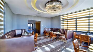 A modern dining area with a chandelier, leather booths, wooden tables, and chairs.