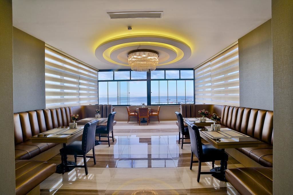 A restaurant with a view of the sea, featuring leather booths, a chandelier, and a polished floor.