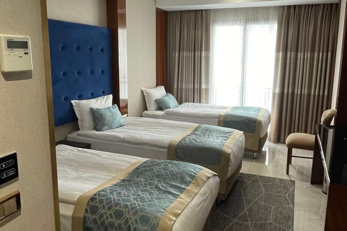 A hotel room with three beds, a television, a control panel, and a window with curtains.